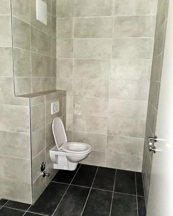 WC-Bereich mit grauen Wand- und dunklen Bodenfliesen – Fliesenleger, Kärnten